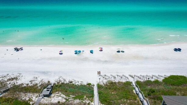 A beach with clear turquoise waters, a sandy shore, and a wooden boardwalk leading to a dune area.