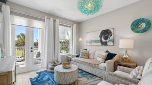A spacious living room with a large window, a round coffee table, a sofa, and a painting of a dog.