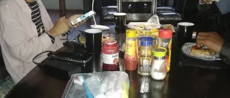 A dining table with condiments, a black mug, and a plate with food.