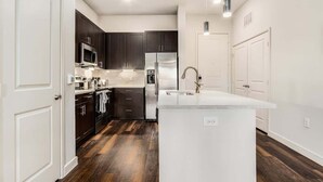 Une cuisine moderne avec des meubles de couleur sombre, des appareils en acier inoxydable et un îlot central blanc.