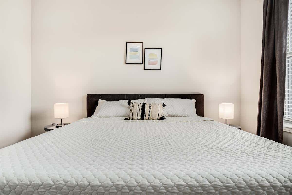A neatly made bed with a white quilt, two bedside lamps, and a pillow with a striped pattern.