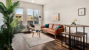 A spacious living room with a leather sofa, a coffee table, and a dining area with a small table and chairs. - Boulevard Stays Trail Access, Plus Parking, Pool, and Gym! (RICHARDSON)