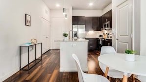 A modern kitchen with dark cabinets, a central island, and a dining area with a white table and chairs. - Boulevard Stays Direct Trail Access! Parking, Pool, Gym 04 (RICHARDSON)