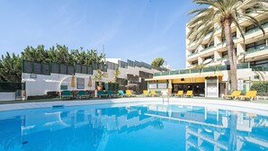 Una piscina con sillas de descanso y un edificio con balcones.