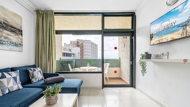 Una sala de estar moderna con un sofá azul, una mesa de centro blanca y vistas de la ciudad a través de un amplio ventanal corredero.