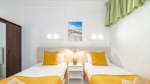 Habitación de hotel con dos camas, una mesita de noche, una pequeña mesa con una planta y vistas al exterior.