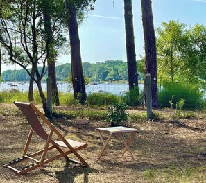 An outdoor seating area with a wooden chair and a small table, surrounded by trees and a view of a lake.