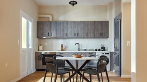 A modern kitchen with grey cabinets, a round dining table with four chairs, and a hanging light fixture. - City Center Sea view Apartment  (Iraklio)
