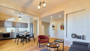 A modern living room with a grey sofa, a red armchair, and a small coffee table. There is a kitchen area with grey cabinets and a dining table with chairs. - City Center Sea view Apartment  (Iraklio)
