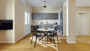 A modern kitchen with grey cabinets, a built-in oven, and a washing machine. There is a round table with chairs in the foreground. - City Center Sea view Apartment  (Iraklio)