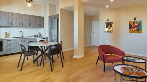 A modern kitchen with wooden cabinets, a dining area with a round table and chairs, a red armchair, and a foosball table. - City Center Sea view Apartment  (Iraklio)