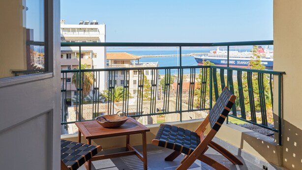 A balcony with a table and two chairs, overlooking a port with a large ship and buildings in the background. - City Center Sea view Apartment  (Iraklio)
