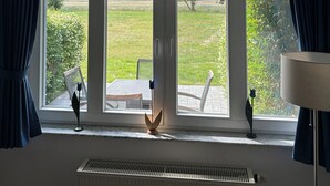 A room with large windows, a radiator, and a table with chairs. - Landhaus am Haff, Apartment B6 - Vacation under thatch (Stolpe auf Usedom)