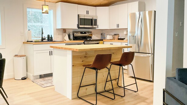 Una cocina moderna con armarios blancos, techo de madera y una isla central con taburetes de bar.