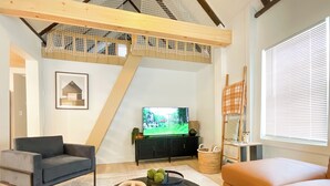 Una sala moderna con televisor, sofá, mesa de centro y una escalera con baranda de malla.