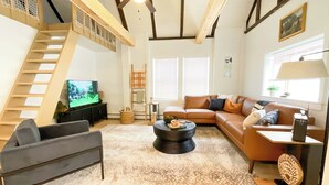 Una sala de estar con sofá, mesa de centro, televisor y una escalera.