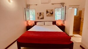 A bedroom with a large bed, two bedside tables with lamps, a window with curtains, and a door leading to another room. - Peaceful villa with garden and swimming pool - 300 m from the beach (Las Terrenas)