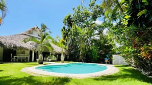 A backyard with a swimming pool, surrounded by lush greenery and a thatched-roof structure. - Peaceful villa with garden and swimming pool - 300 m from the beach (Las Terrenas)
