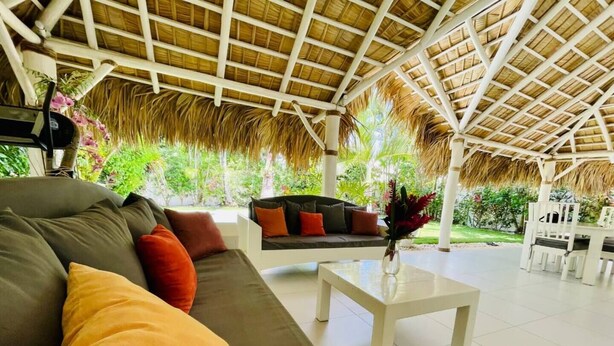 An open-plan living area with a thatched roof, a sofa set, and a dining table. - Peaceful villa with garden and swimming pool - 300 m from the beach (Las Terrenas)