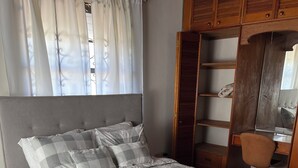 Ein ordentlich bezogenes Bett mit karierter Tagesdecke, ein Nachttisch und ein Stuhl.