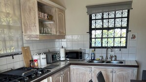 Eine Küche mit einer zentralen Kochinsel, einem Essbereich mit Tisch und Stühlen, einem Fenster mit dekorativen Eisenverzierungen und einer gefliesten Spritzschutzwand.