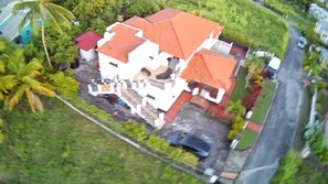An aerial view of a house with a red-tiled roof, surrounded by lush greenery and a paved driveway. - Cozy place with WiFi, AC ,close to beach. Free loaner car avail. (Saint James)