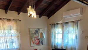 Ein Wohnzimmer mit einem roten Sofa, einem blauen Sofa und einem Glastisch. Es gibt einen Deckenventilator, eine Klimaanlage und ein Gemälde an der Wand.