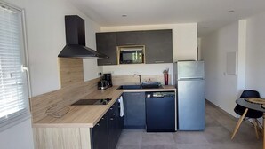 A modern kitchen with a built-in microwave, a stainless steel refrigerator, a sink, and a small dining area with two chairs. - Apartment 7 minutes from Porto Vecchio (Porto-Vecchio)