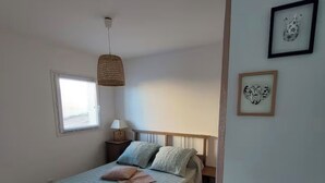 A bedroom with a bed, a window, a hanging light fixture, and framed artwork on the wall. - Apartment 7 minutes from Porto Vecchio (Porto-Vecchio)