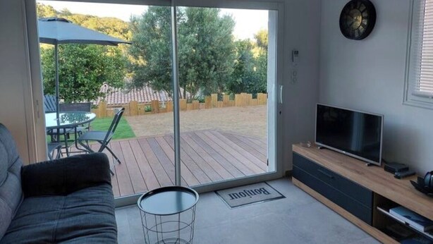A modern living room with a sofa, a TV on a wooden stand, and a sliding glass door leading to an outdoor deck. - Apartment 7 minutes from Porto Vecchio (Porto-Vecchio)