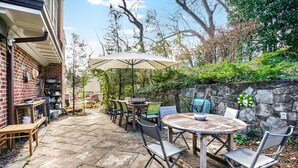 A patio with a stone table and chairs, a wooden bench, and a large umbrella. - Grand 5200 sf Home, Wesley Heights, 4BR 3.5BA (Washington)