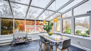 A conservatory with a table and chairs, a cart with bottles, and a view of trees and a house. - Grand 5200 sf Home, Wesley Heights, 4BR 3.5BA (Washington)