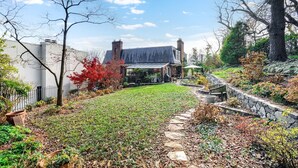 A backyard with a stone pathway, a brick house, and a fenced area. - Grand 5200 sf Home, Wesley Heights, 4BR 3.5BA (Washington)