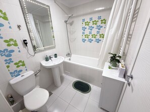 Features a bathtub, standalone sink, and toilet, plus a small shelf for toiletries.