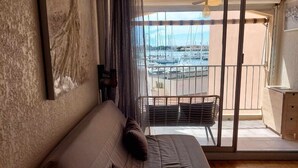 Une chambre dotée d’un grand lit, offrant une vue sur une marina grâce à une porte-fenêtre coulissante, et disposant d’un balcon avec un fauteuil.
