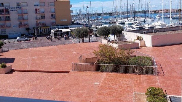 Un port de plaisance où sont amarrés de nombreux voiliers, un bâtiment d’hôtel doté de balcons et une zone pavée agrémentée d’arbres et d’une clôture.