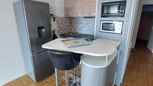 Une cuisine compacte équipée d’un réfrigérateur, d’un four à micro-ondes et d’un petit plan de travail agrémenté d’une chaise.