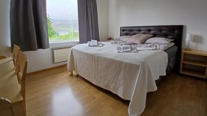 A bedroom with a bed, a chair, a nightstand, and a window with curtains.