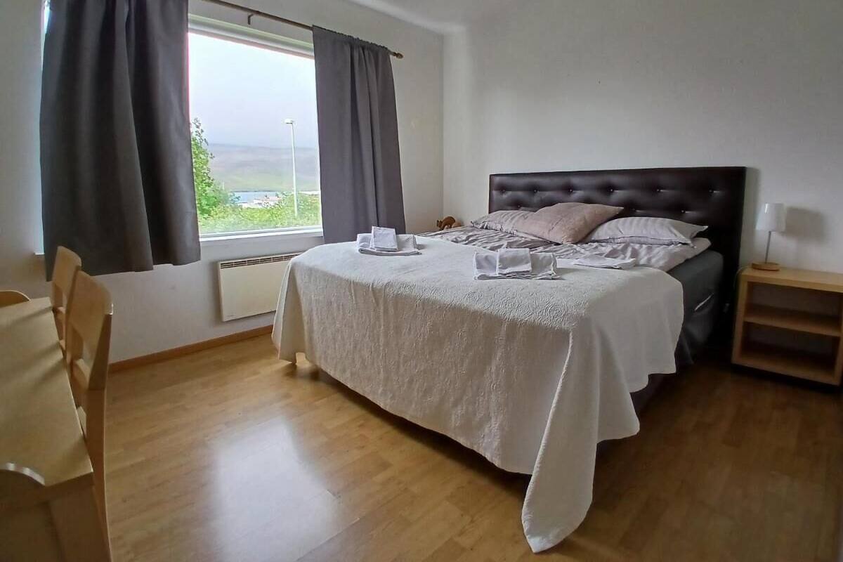 Une chambre à coucher avec un lit, une chaise, une table de chevet et une fenêtre avec des rideaux.