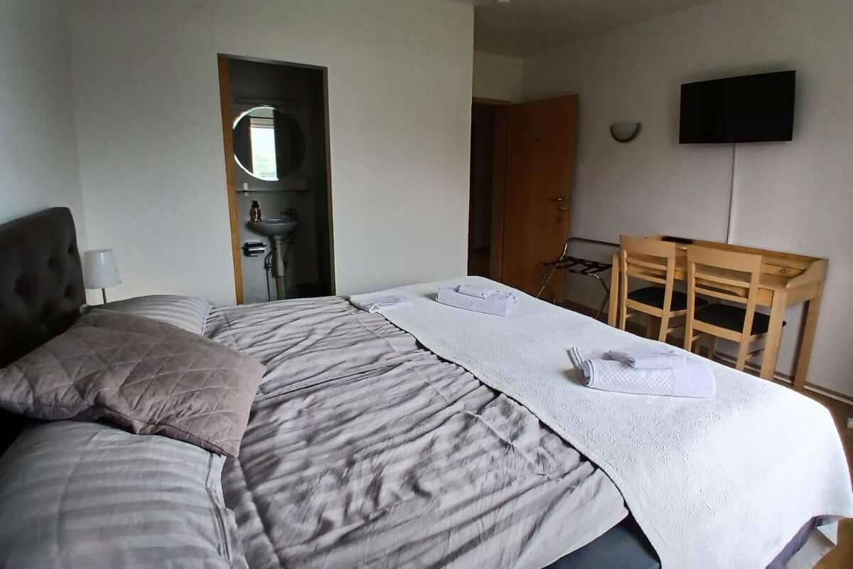 Un lit bien fait, avec des oreillers, une table de chevet, une chaise et un téléviseur fixé au mur.