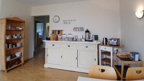 A kitchen with white cabinets, a wooden dining table, and a clock on the wall.