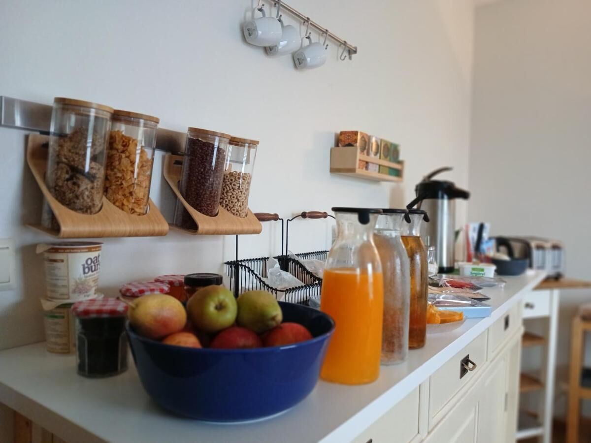 Una encimera de cocina con frascos de cereales, un cuenco de fruta y una botella de jugo de naranja.