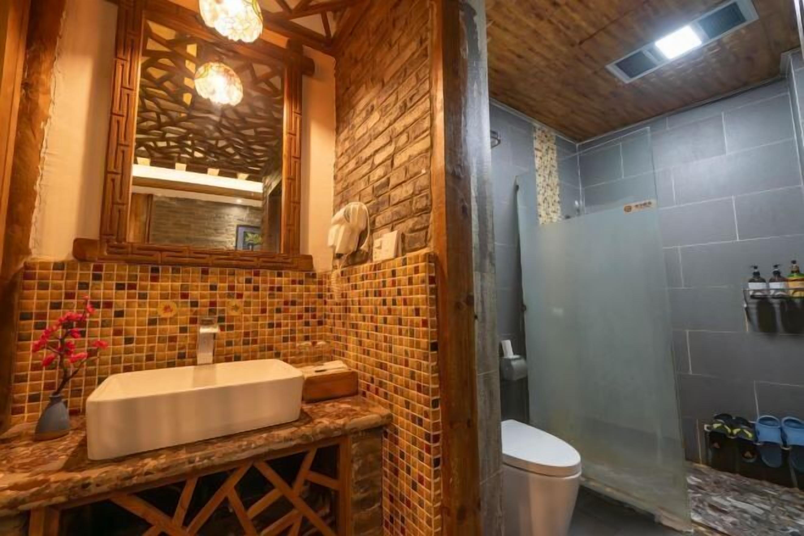 A bathroom with a mosaic tile wall, a wooden vanity, a white sink, and a shower area.