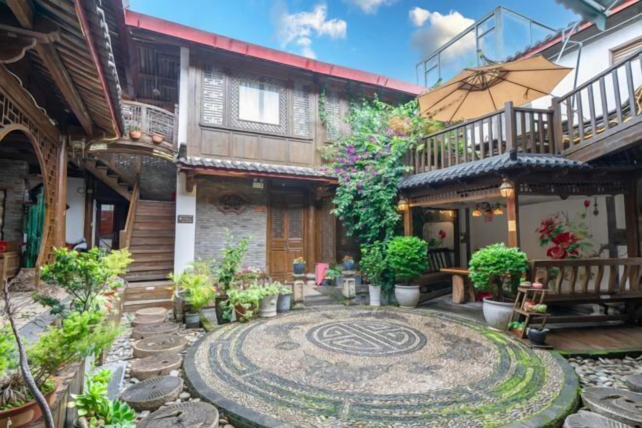 Un patio con suelo de piedra estampado, edificios de madera con balcones y plantas en macetas.