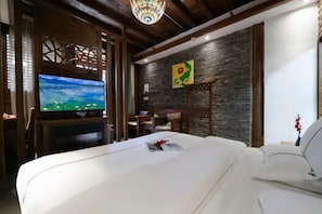 A hotel room with a large bed, a television, a desk, and a stone wall.