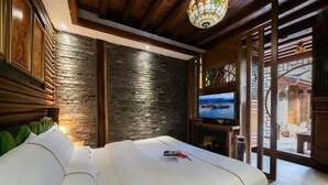 A modern hotel room with a stone wall, wooden ceiling, and a large TV. - Dayetang Private Shangpin Inn (Lijiang) (Lijiang)