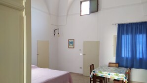 A room with a bed, a table with chairs, a window with curtains, and a door. - Casetta Rita in Melpignano (Melpignano)