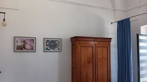 A room with a wooden wardrobe, two framed artworks on the wall, a light fixture, and a blue curtain. - Casetta Rita in Melpignano (Melpignano)