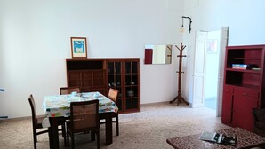 A dining area with a table and chairs, a coat rack, a bookshelf, and a door. - Casetta Rita in Melpignano (Melpignano)