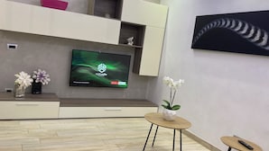 A modern living room with a flat-screen TV, wooden flooring, a coffee table, and decorative vases. - Orchid Apartment (Castiglione Olona)